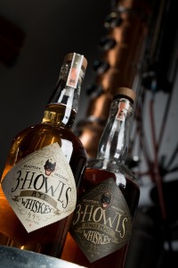 Bottles of 3 Howls Whiskey sit in front of the stills at their distillery in Seattle, WA. Photography by Ari Shapiro - The Whisky Guy